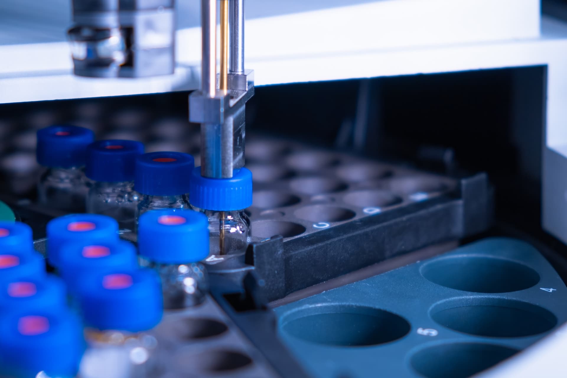 Autosampler needle drawing from a blue-capped vial in an HPLC rack