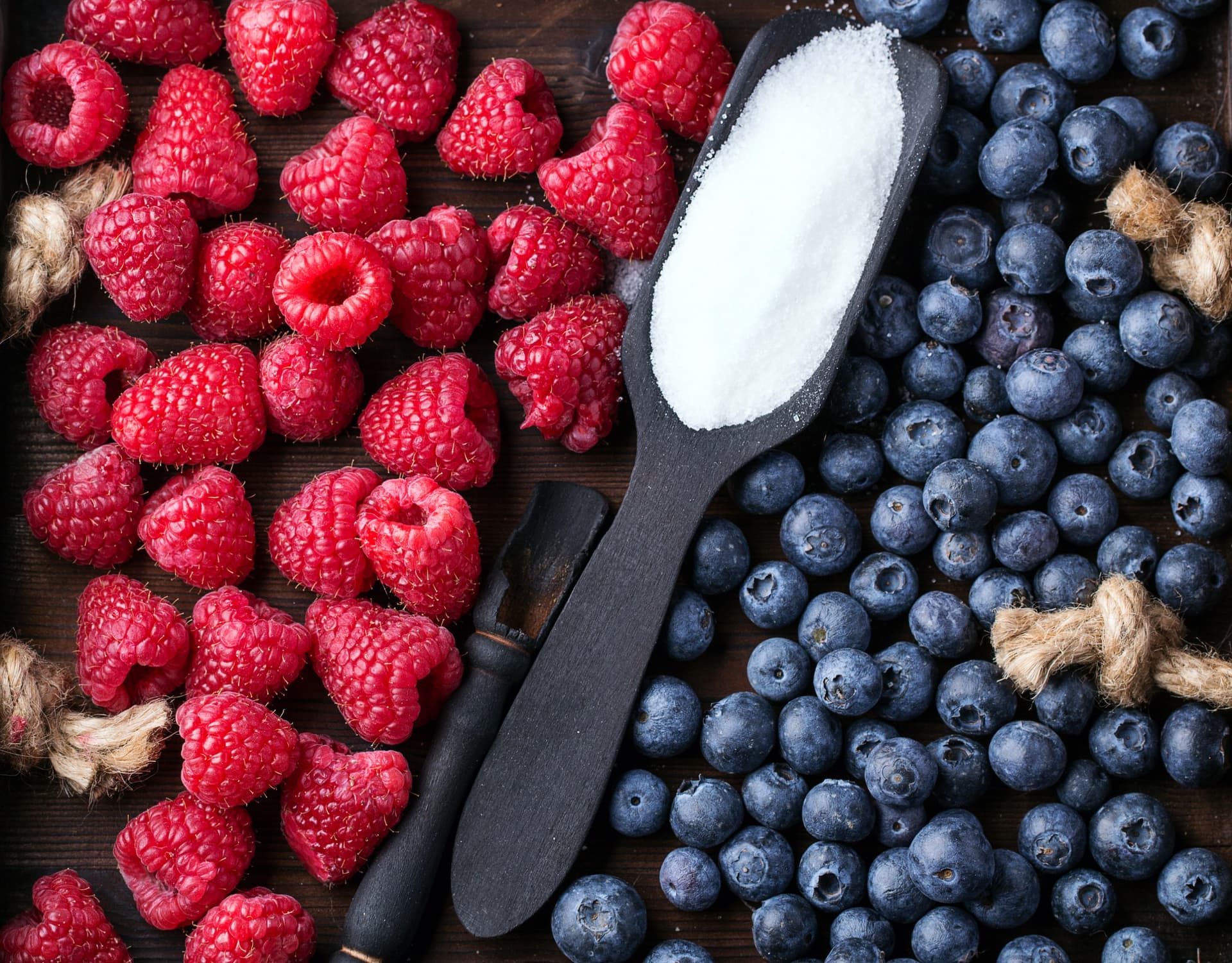 Close-up of raspberries and blueberries with a scoop of sugar