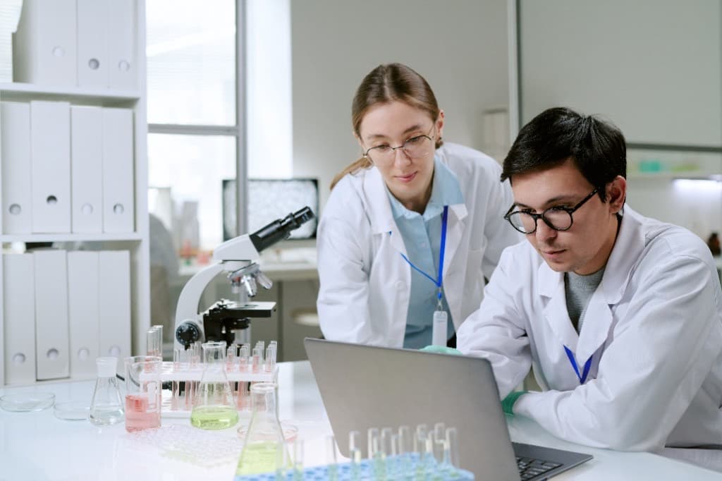 Two scientists working through data on a laptop at a lab bench